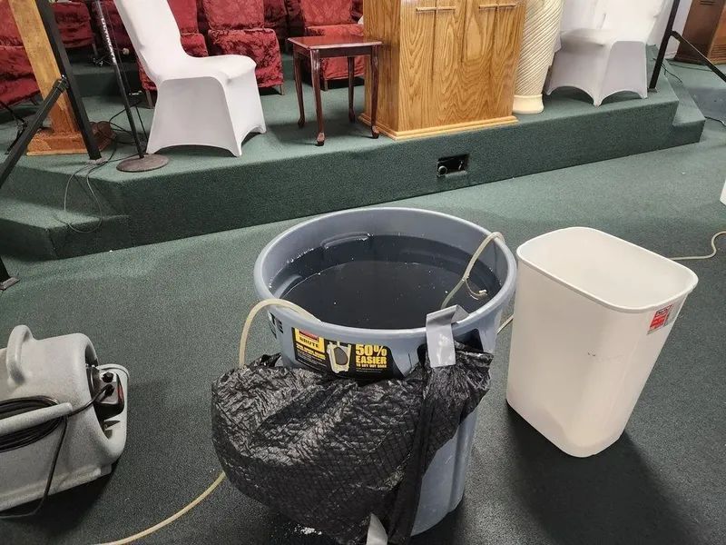 Gray trash can and white bin on carpeted floor in front of a stage with chairs and a podium.
