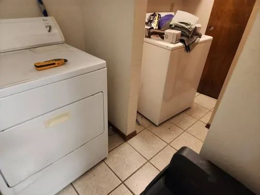 Laundry room with white washer and dryer, tile floor, and a black chair in the foreground