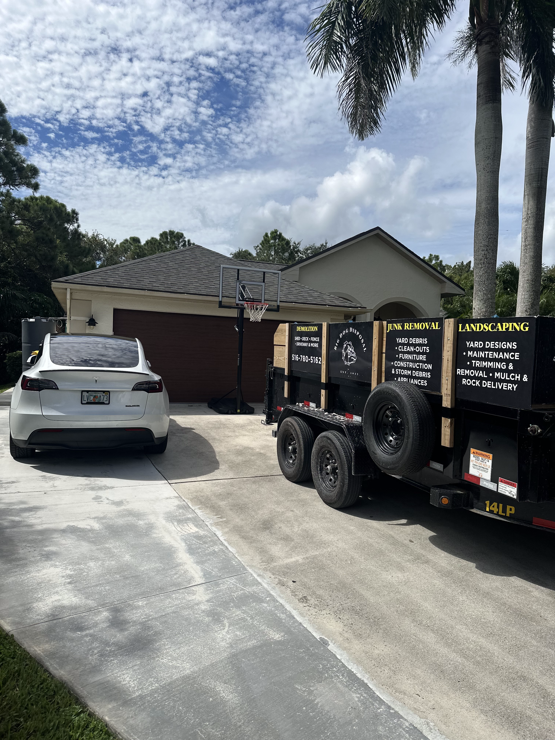 A white car is parked in a driveway next to a dump truck.