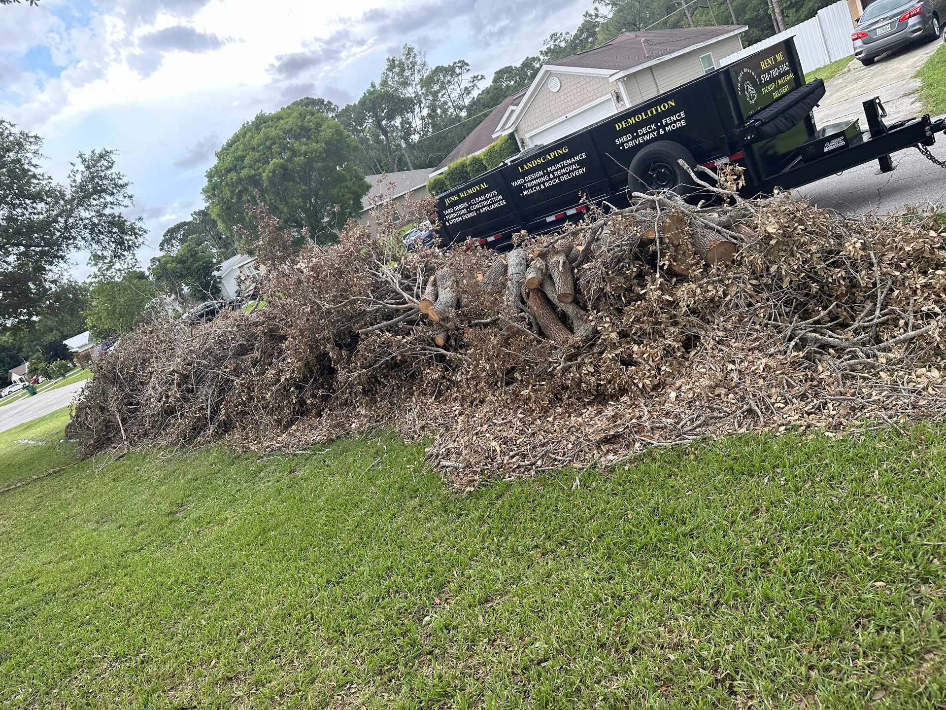 A trailer is carrying a pile of branches on a lush green lawn.