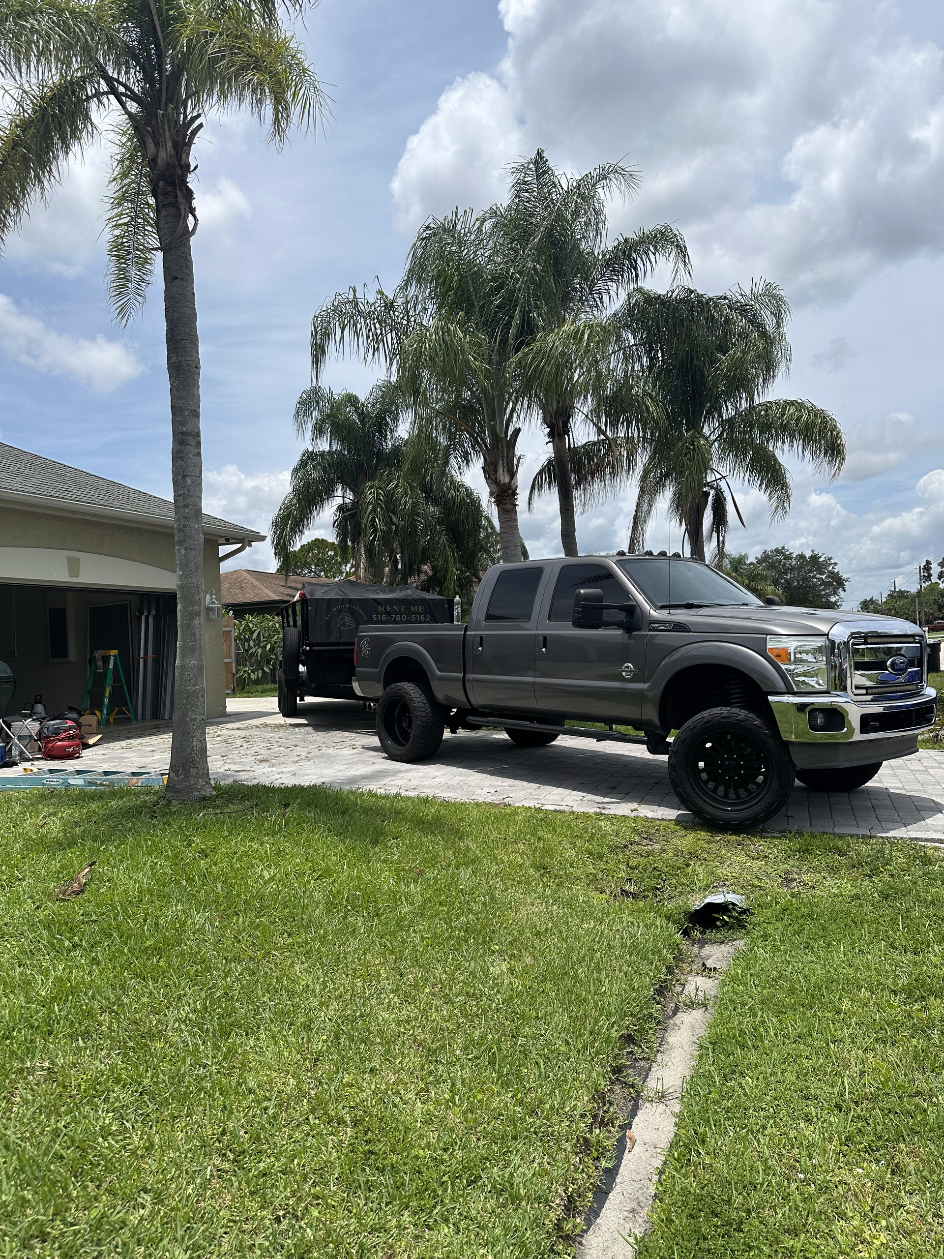 A gray truck is parked in a driveway next to a palm tree.