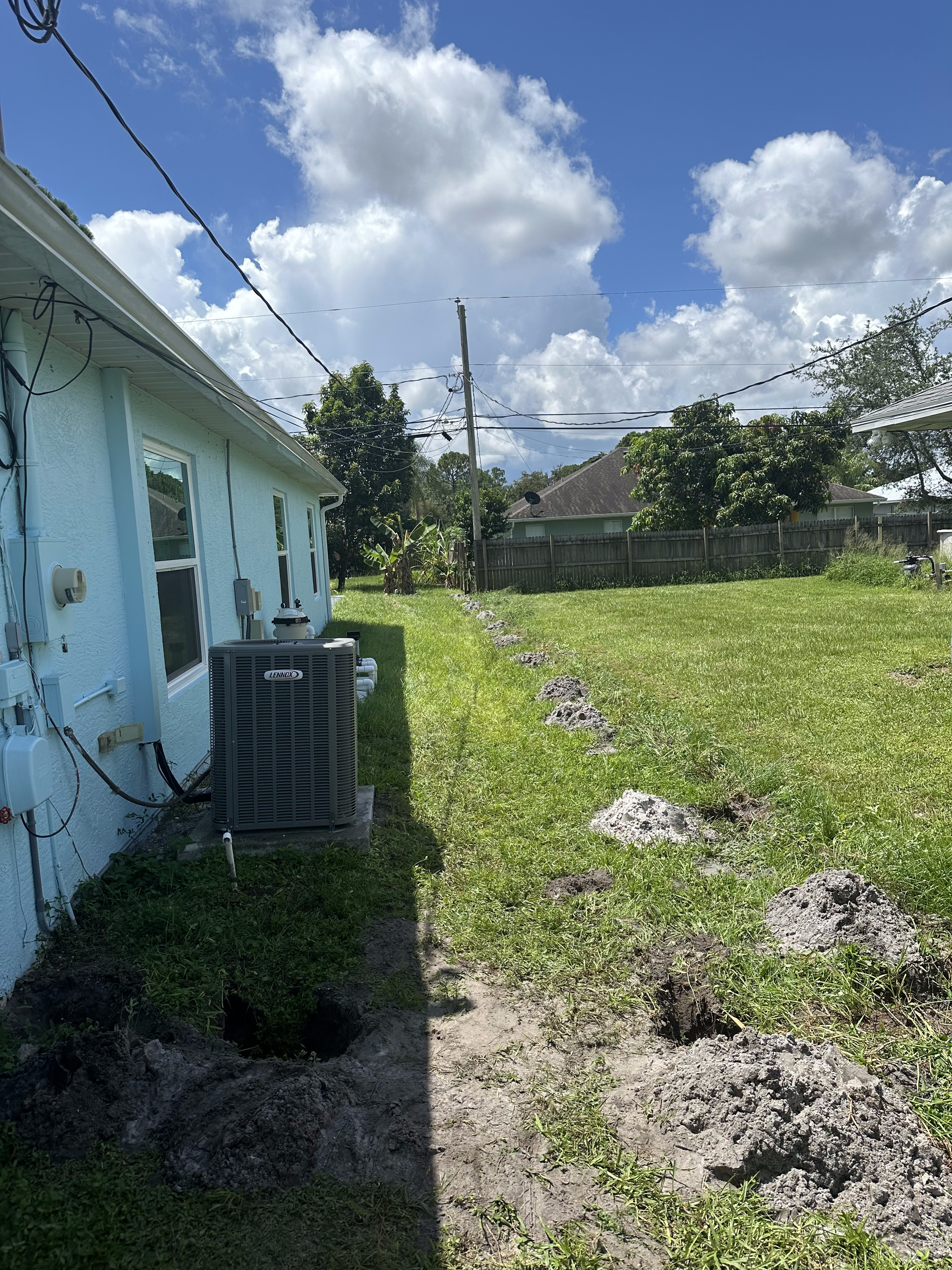 A blue house with a gray air conditioner in the backyard.