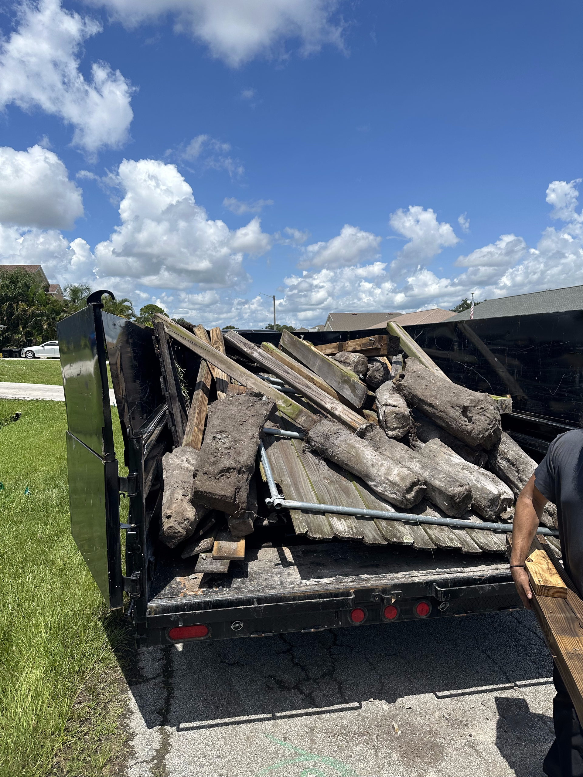 A man is standing next to a dumpster filled with wood.