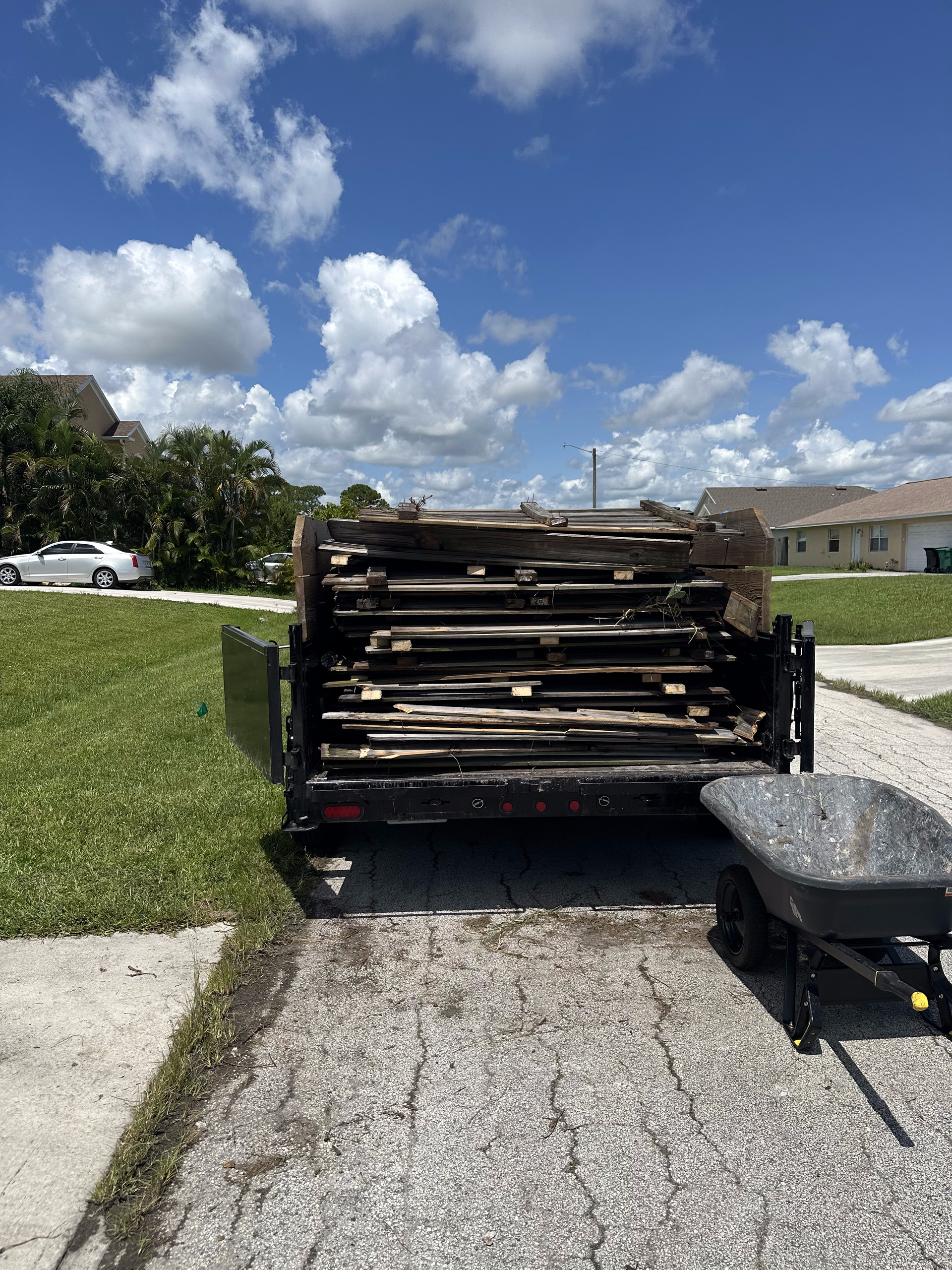 A wheelbarrow is sitting next to a trailer filled with wood.