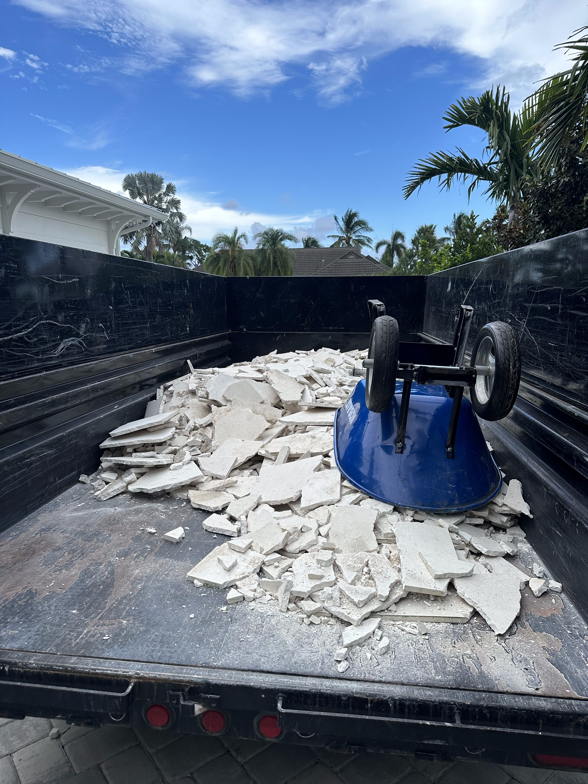 A dumpster filled with broken tiles and a wheelbarrow.