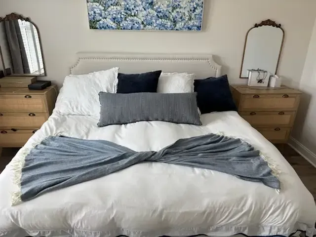 Neatly made bed with white bedding, gray throw, navy pillows, and matching wooden nightstands in a cozy bedroom.