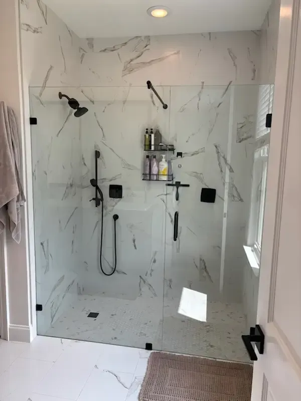 Modern walk-in shower with marble-look tile, black fixtures, and built-in shelf with toiletries