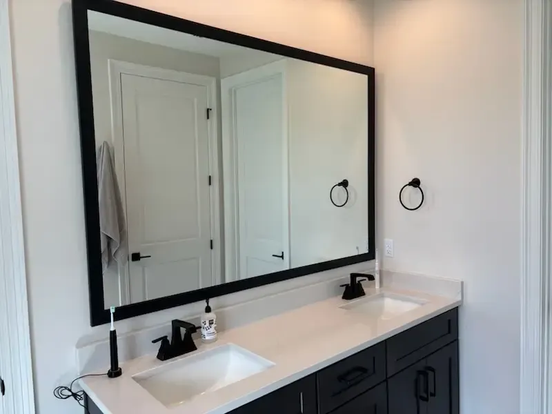 Modern bathroom vanity with double sinks, large black-framed mirror, and wall sconces