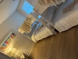 Tilted view of a cozy bedroom with bunk beds, wooden floor, and a window with patterned curtains