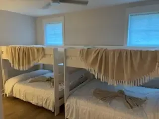 Two bunk beds in a simple bedroom with beige blankets and blue windows overhead