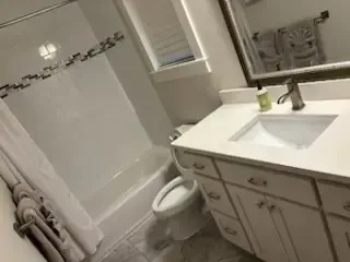 Bathroom with white tub, toilet, and vanity sink in a bright, tiled interior.
