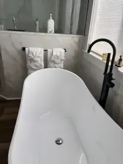 Modern bathroom with a white freestanding bathtub and black faucet near a tiled shower wall