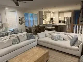 Bright living room with two light gray sofas, wooden coffee table, and open kitchen in the background