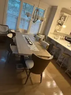 Modern dining room with a long table, chairs, and warm lighting beside a kitchen counter.
