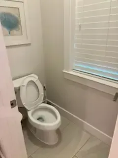 Small bathroom with an open toilet beside a window with white blinds.
