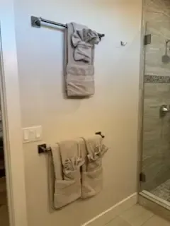 Hotel bathroom wall with towels on chrome racks near a glass shower stall.