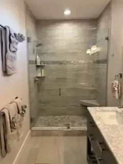 Modern bathroom with glass shower, marble vanity, beige tile, and towels on wall racks