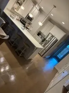 Modern kitchen with white cabinets, island seating, and stainless steel appliances, viewed at an angle.