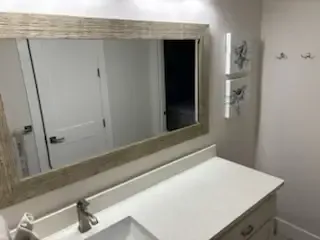 Bathroom vanity with large mirror, white countertop, and wall decor beside a closed door.