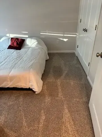 Small bedroom with a bed, red pillow, beige carpet, and white closet doors.