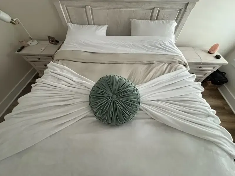 Neatly made bed with white bedding and a green decorative pillow in the center