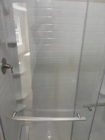 Glass shower enclosure with chrome grab bars and towel bars in a tiled bathroom.