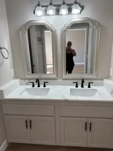Double vanity bathroom with two mirrors, black faucets, and a person reflected in the center mirror