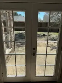 French doors with glass panes opening to a sunny backyard patio and yard