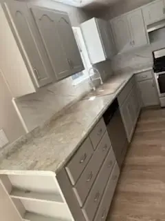 Empty modern kitchen with beige cabinets, granite countertops, and white appliances viewed at an angle