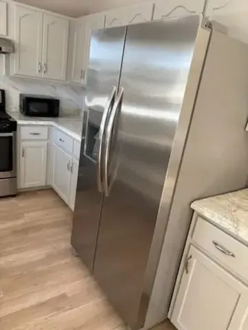 Stainless steel side-by-side refrigerator in a bright white kitchen with light wood floors.