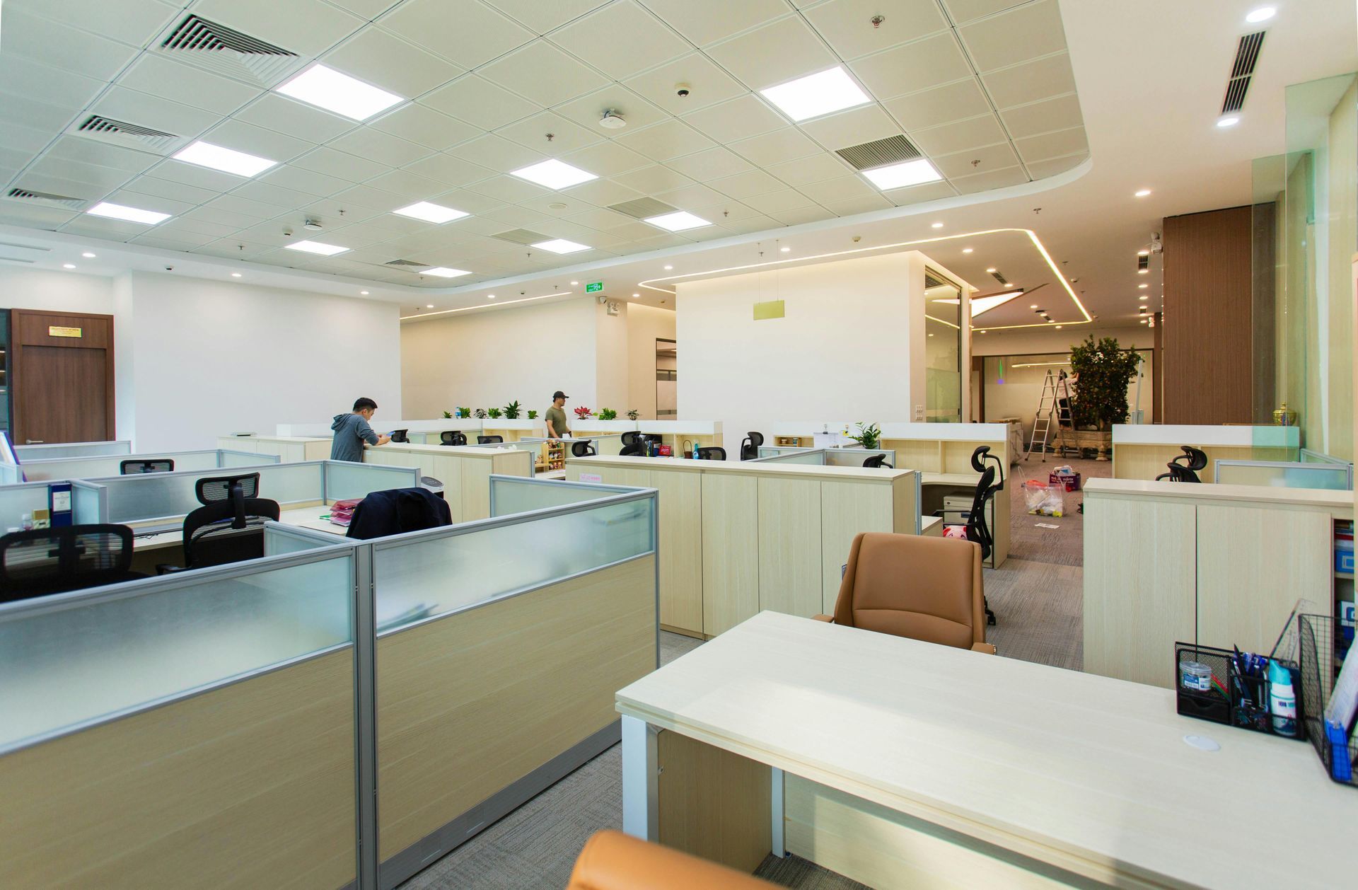 Modern open-plan office with beige cubicles, desks, and bright ceiling lights