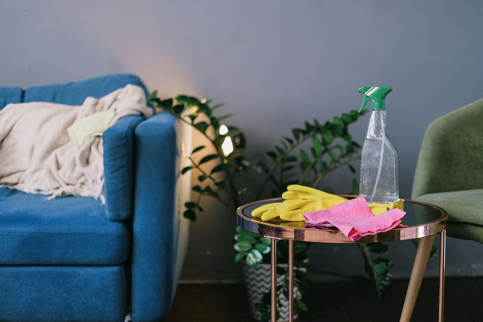 Living room with blue sofa, side table, spray bottle, and colorful cleaning cloths