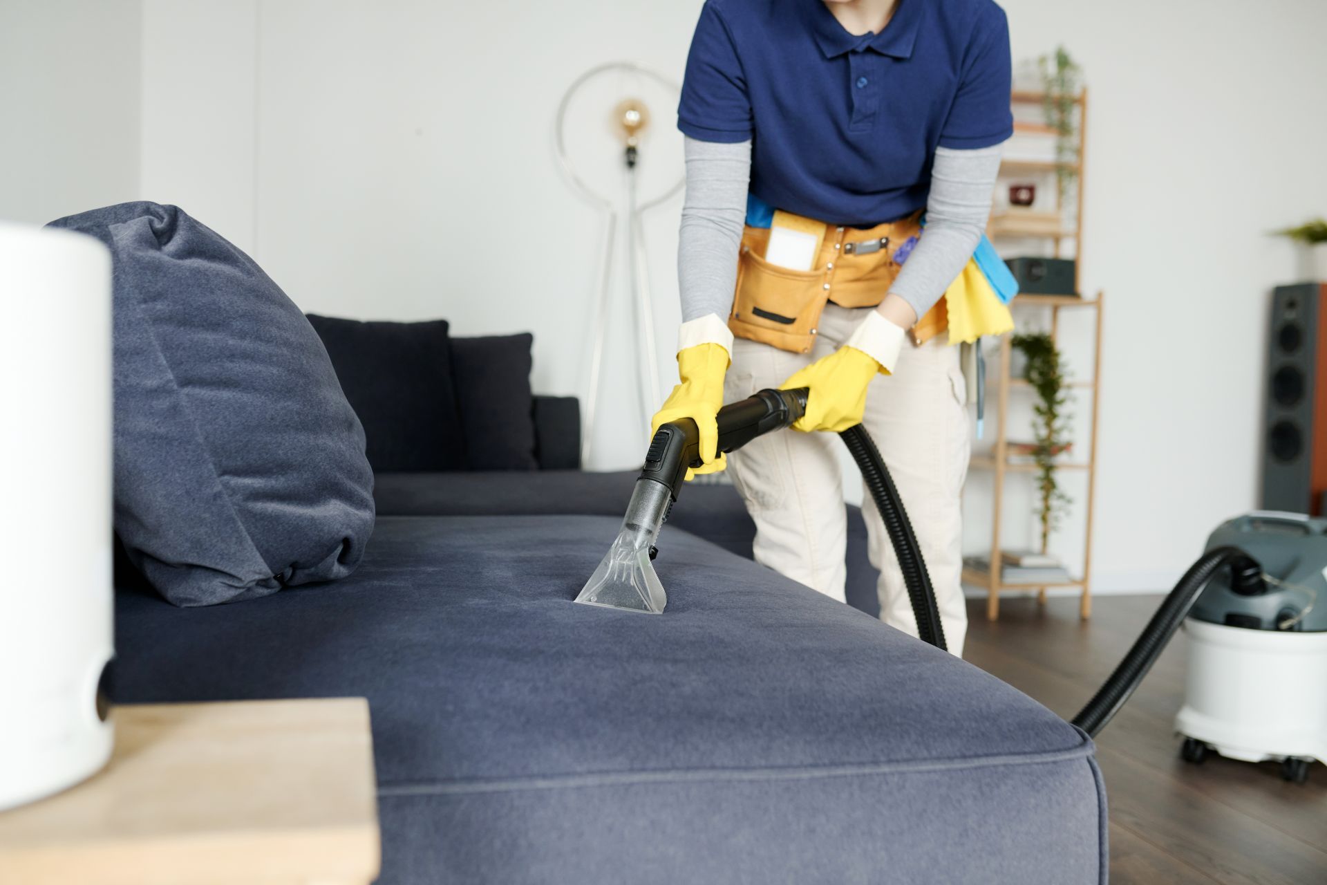 Person cleaning a blue sofa with a vacuum in a bright living room