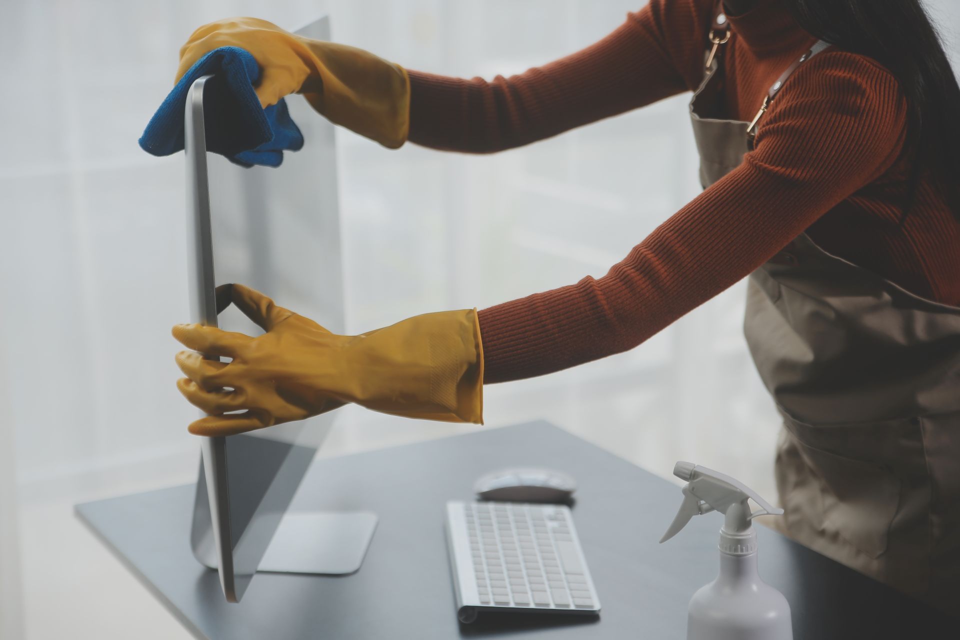 Person assembling a flat-screen monitor on a desk, with keyboard and spray bottle nearby