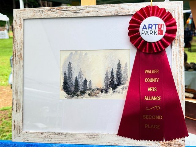 Award-winning watercolor painting in white frame with red first-place ribbon and rosette outdoors