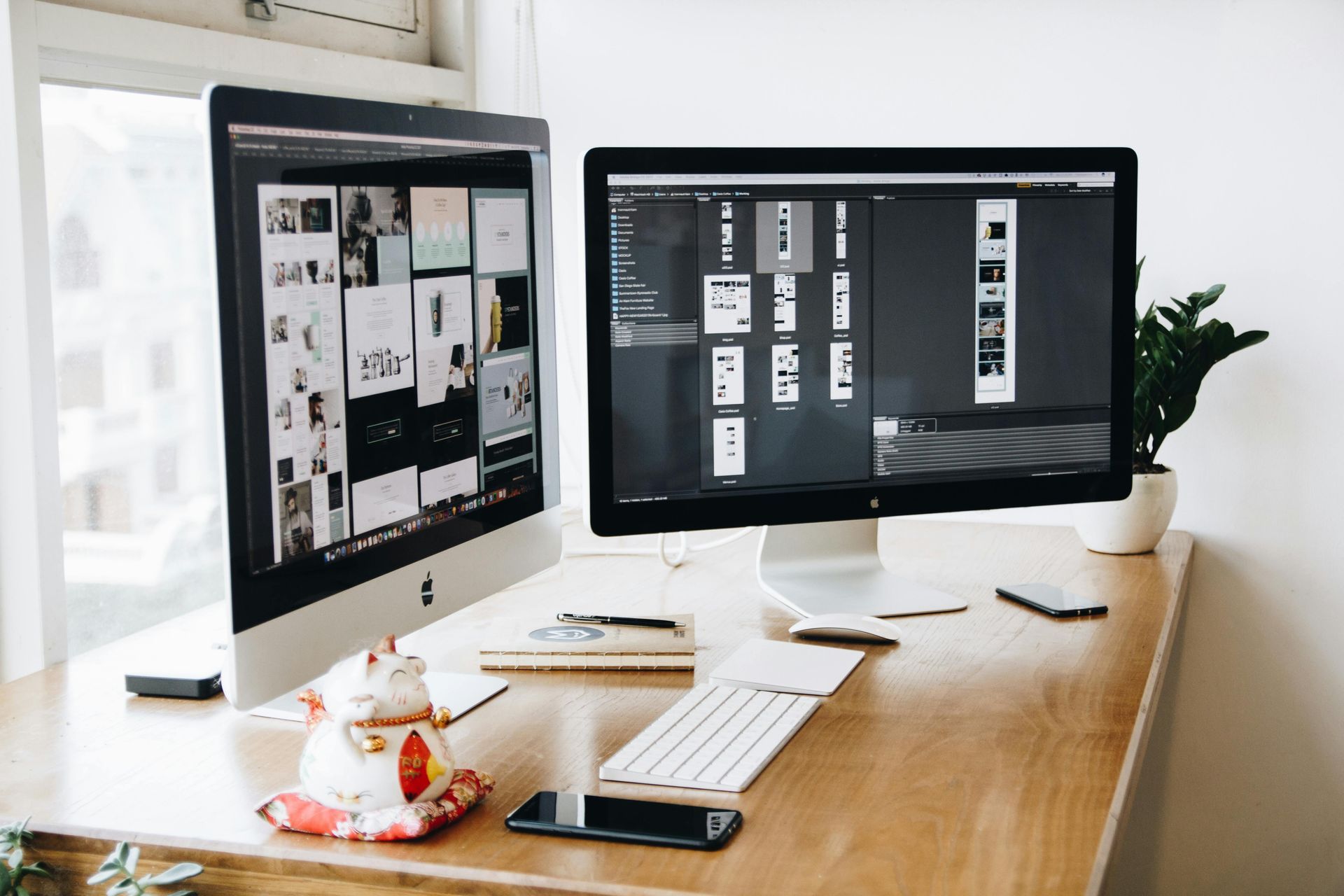 Two computer monitors on a wooden desk, one displaying a design layout, the other a list of images, with a small plant.