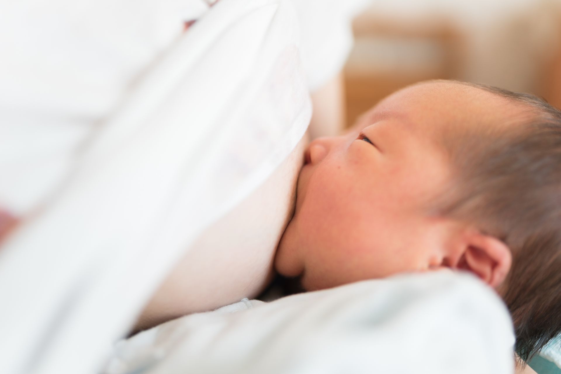 Newborn sleeping against a white blanket, eyes closed, in soft warm light