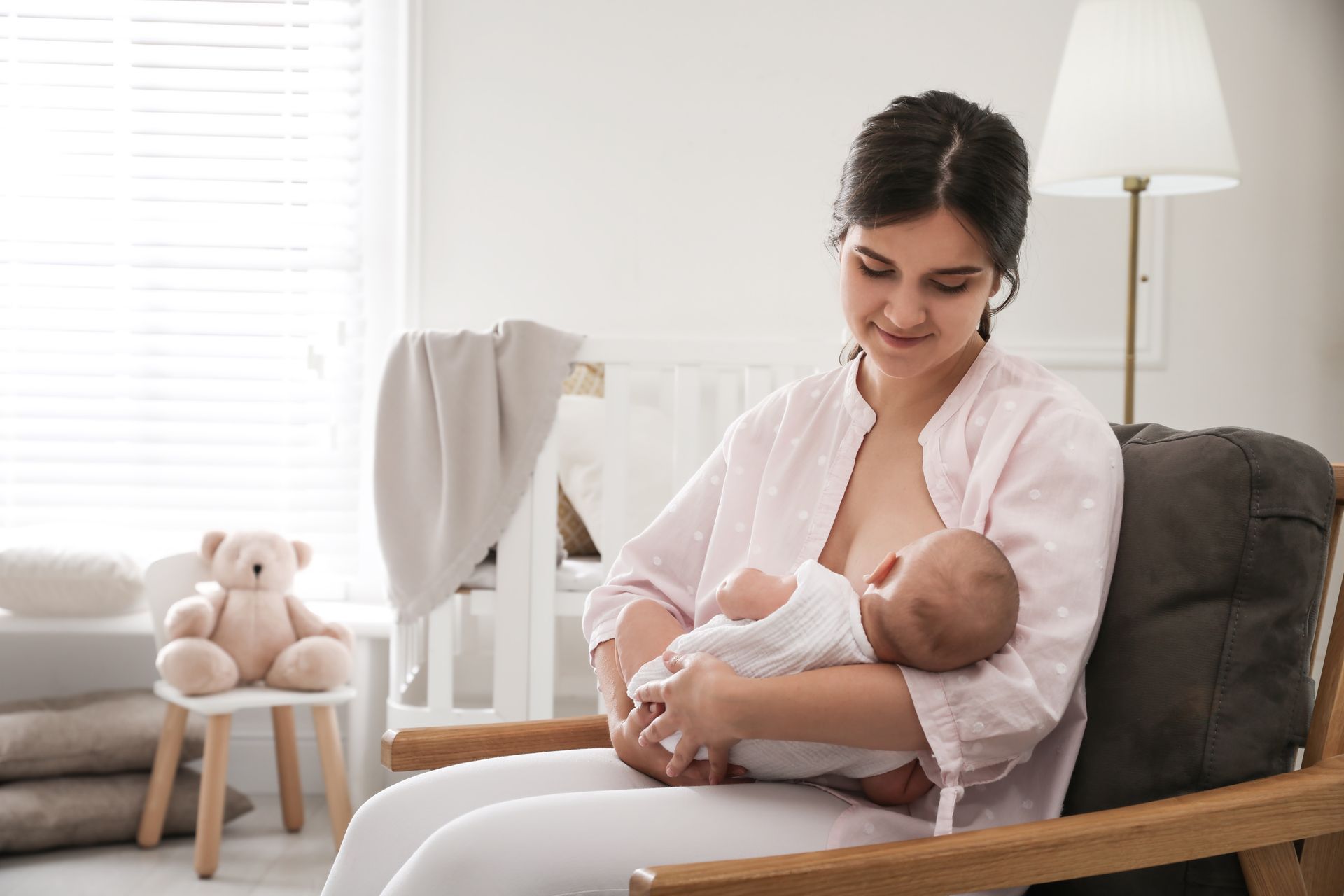 Woman sitting in a chair, cradling a baby in a bright nursery by a window