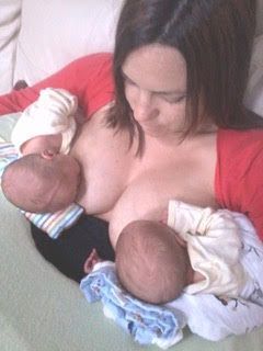 Woman breastfeeding twins, holding one baby at each breast on a bed.