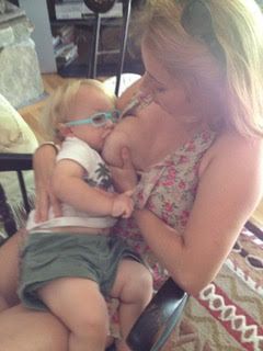 A woman kisses a baby wearing glasses and a white top while holding them indoors.
