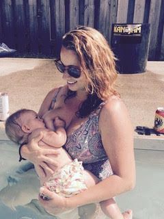 Woman in sunglasses cradling a baby in a swimsuit by a poolside trash can