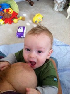 Baby sitting on the floor in a playroom, touching a ball, with colorful toys scattered nearby.