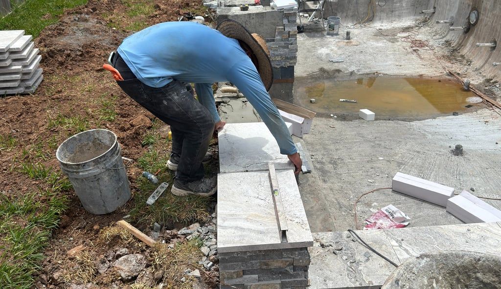 Worker in blue shirt and black pants laying white paving stones at a muddy construction site