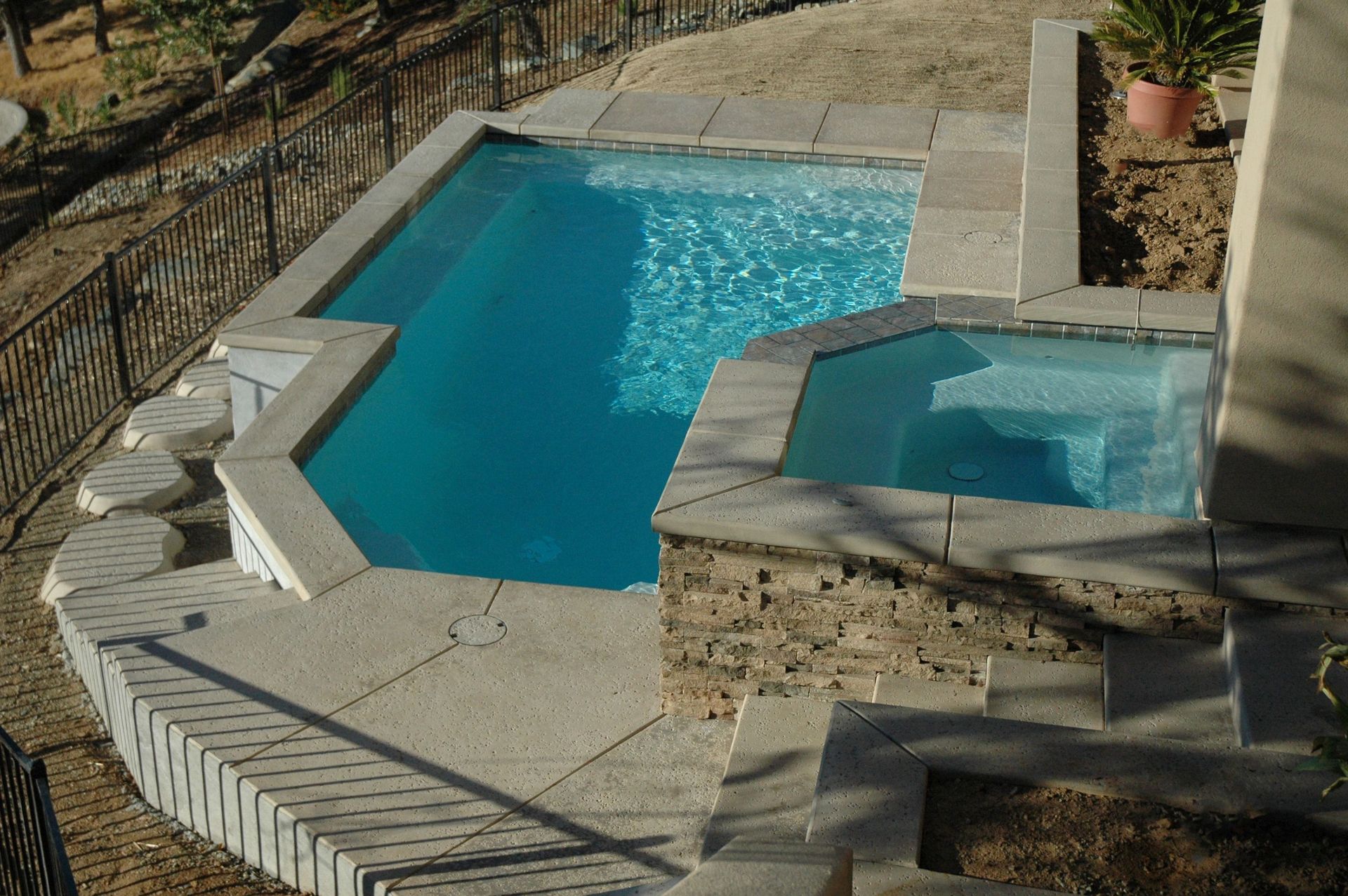 Stone patio with a blue backyard swimming pool and attached hot tub