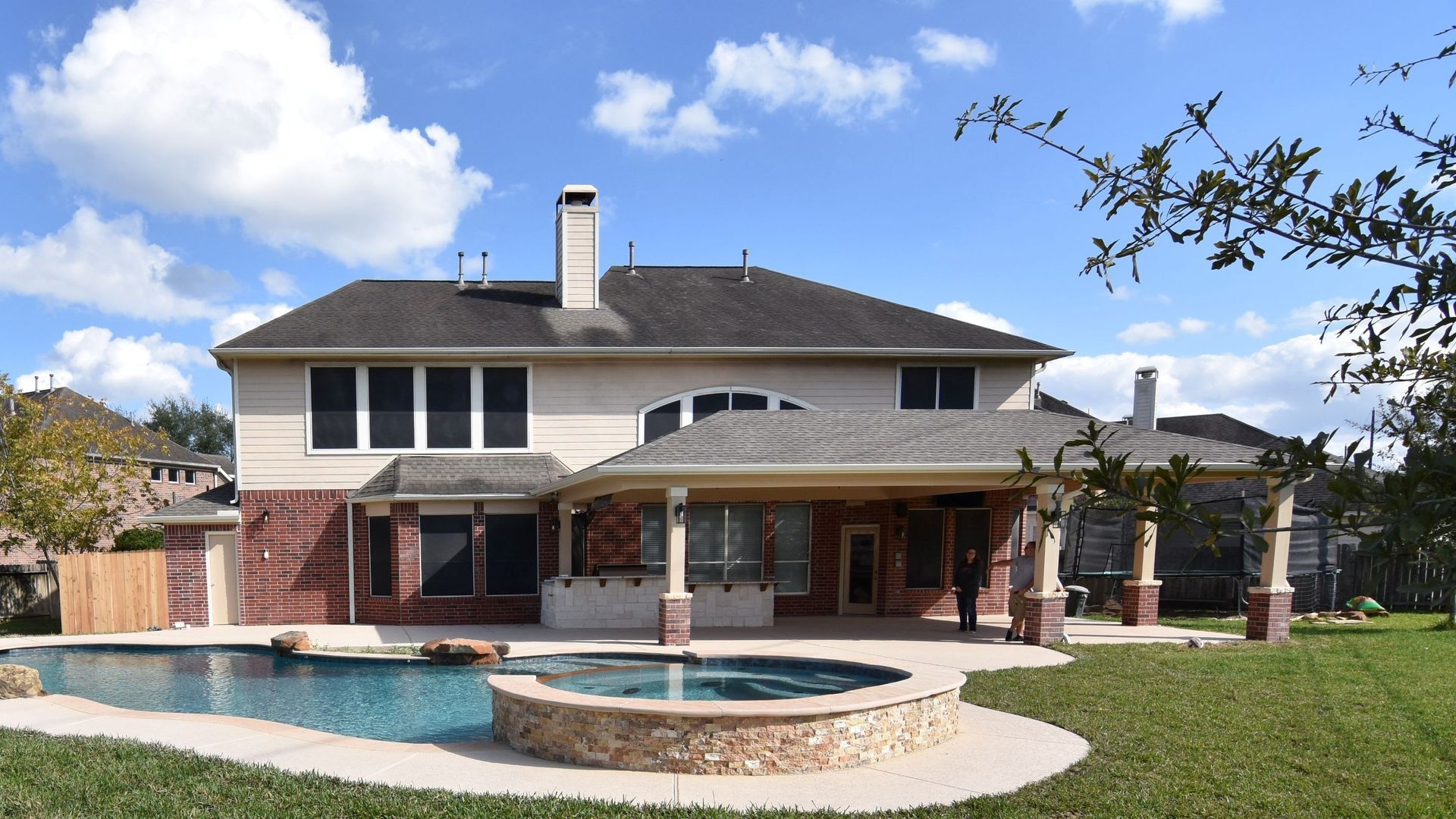Two-story suburban house with a covered patio and a backyard pool and spa under a blue sky