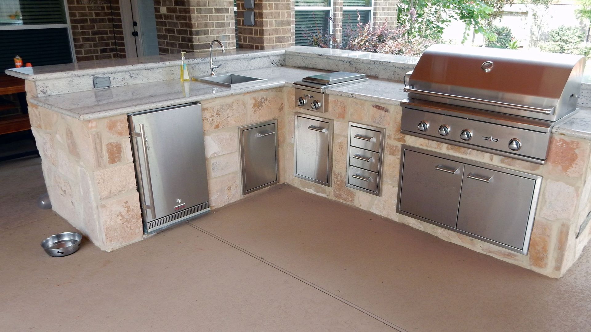 Outdoor stone patio kitchen with stainless steel grill, sink, and cabinets under a countertop
