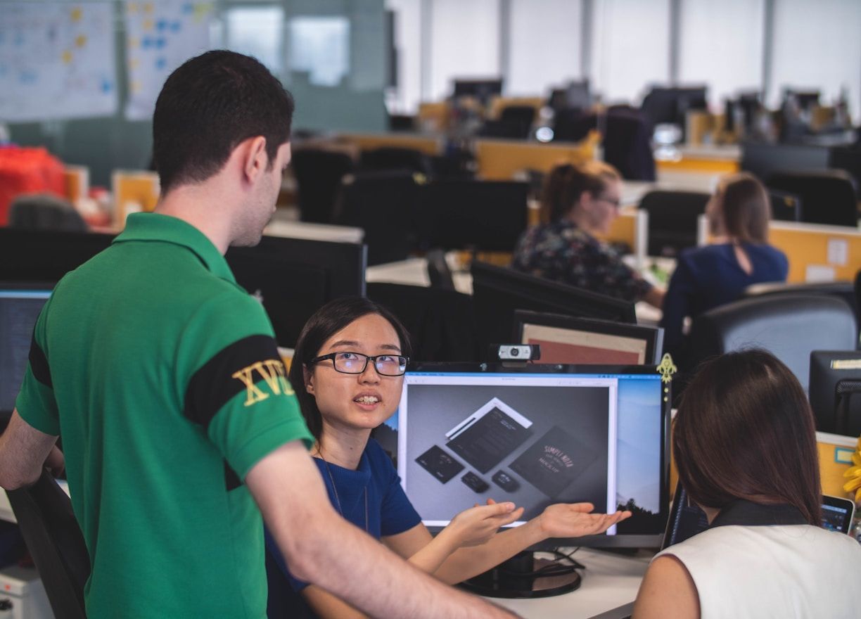 People collaborating in a computer lab, with one person pointing at a monitor displaying a design.