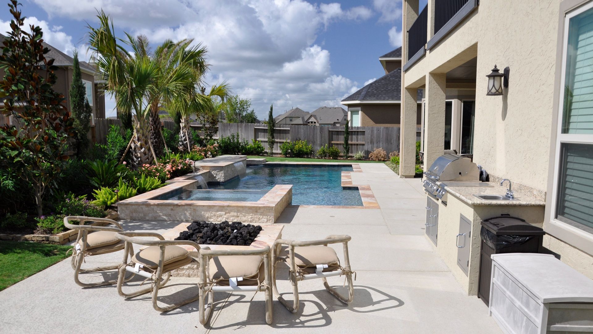 Modern backyard patio with pool, fire pit seating, grill, and a view of a house and palm trees