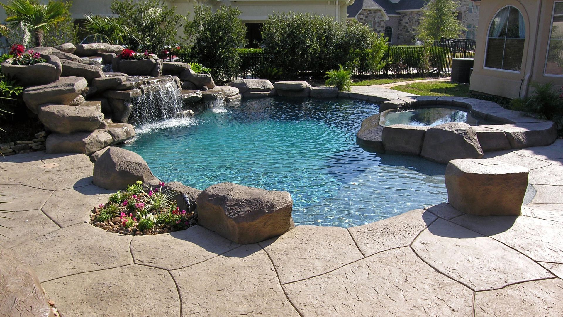 Backyard pool with rock waterfall, blue water, and stone patio in sunlight