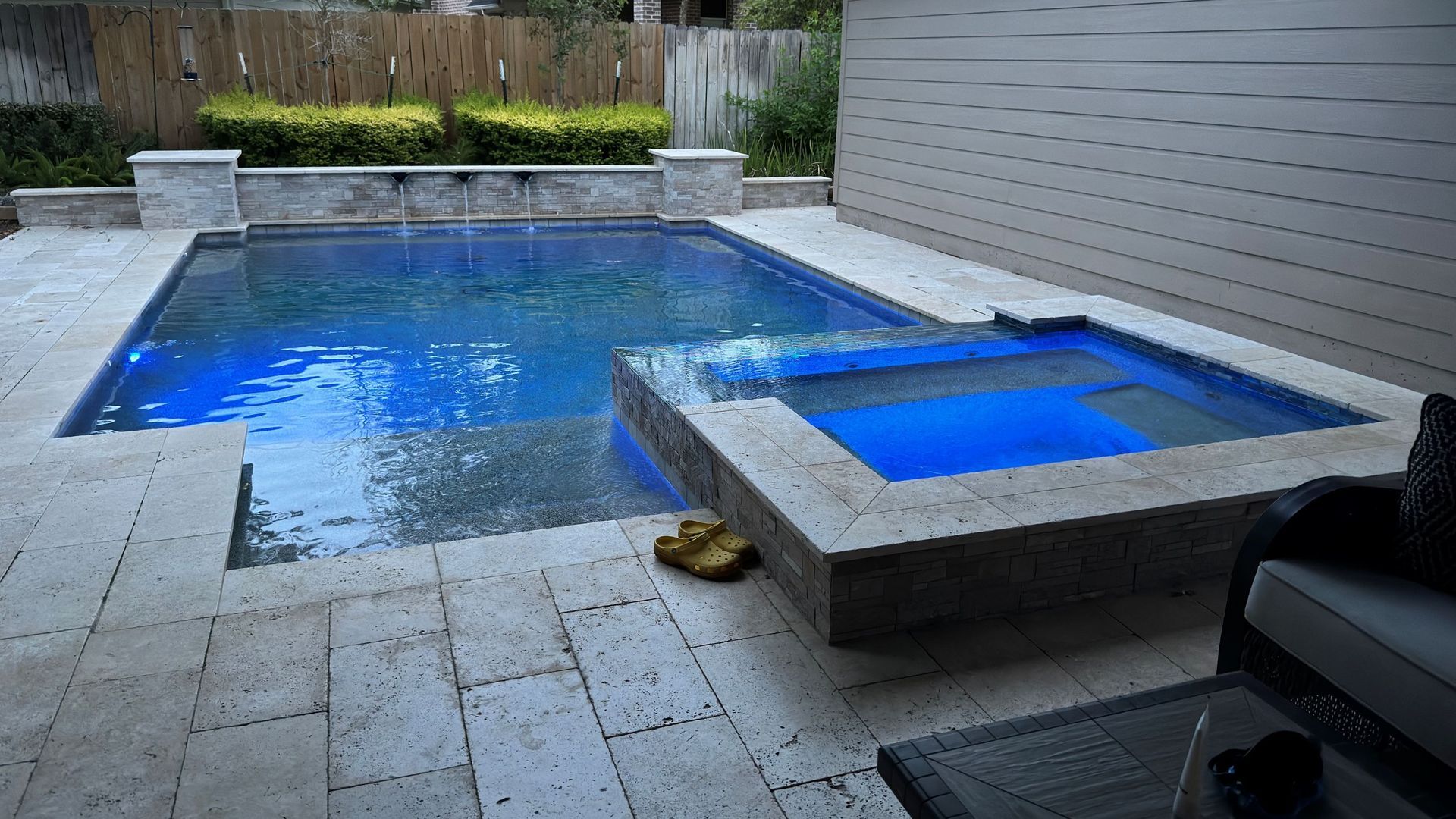 Backyard patio with a blue swimming pool and small raised spa beside a stone deck